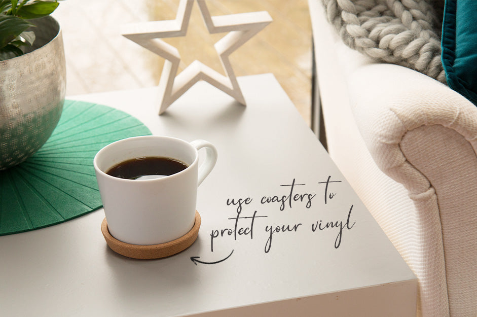 Vinyl covered side table in grey matte with cup of coffee and text pointing to coaster saying: use coasters to protect your vinyl