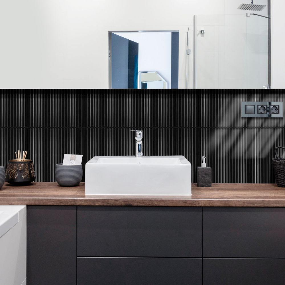 Modern bathroom with a white sink on a wooden countertop, black tiles on the wall, and a mirror.