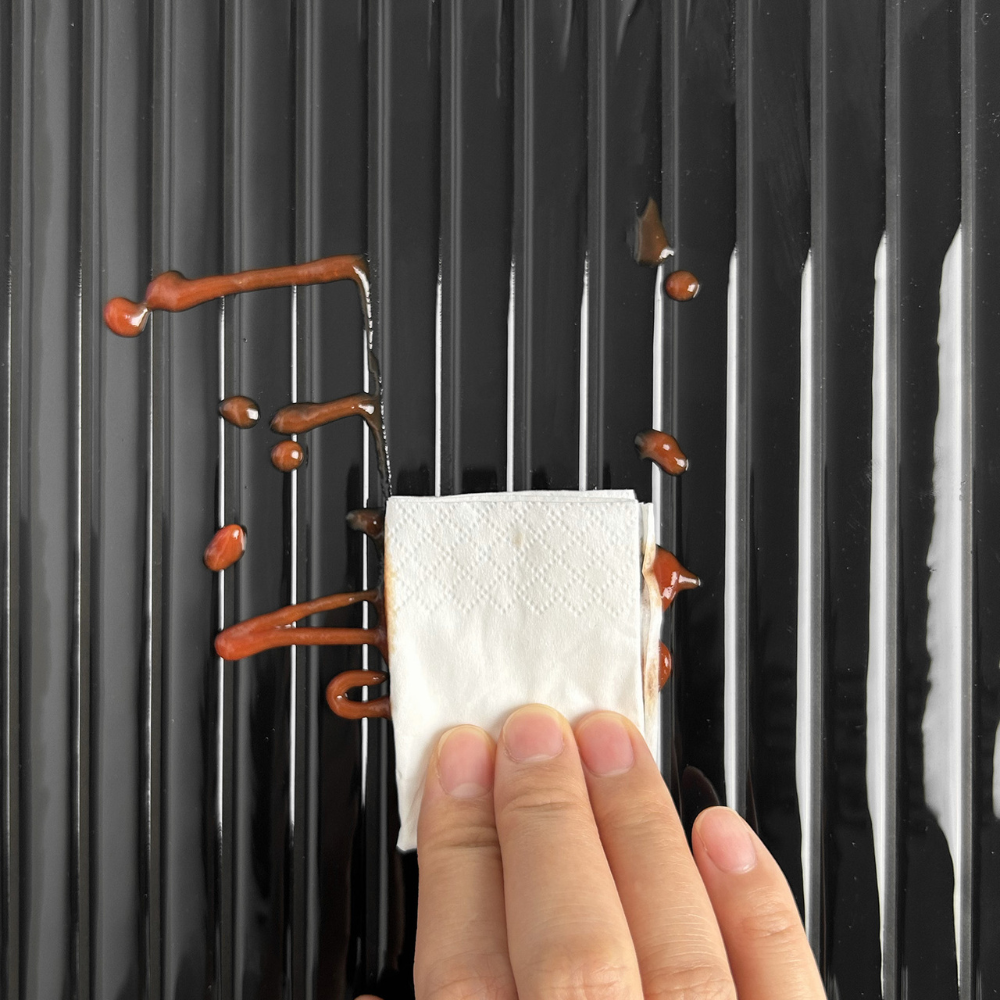 Hand wiping sauce off a black reeded tile with a white napkin.