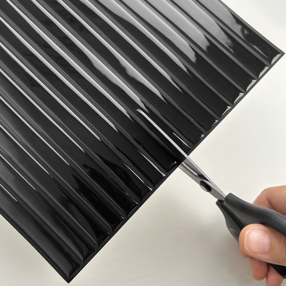 Person cutting a black reeded tile with scissors on a white background