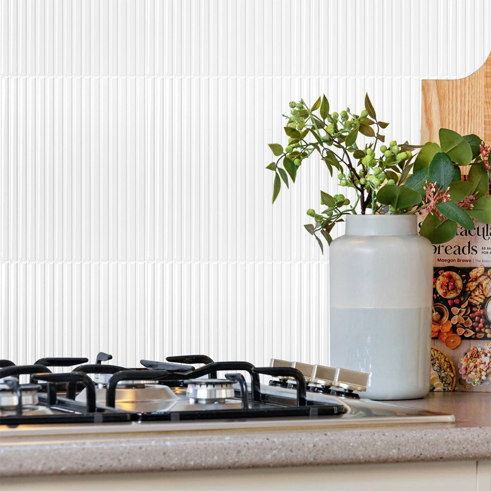 Kitchen counter with a vase of greenery and a cookbook against a white tiled wall.