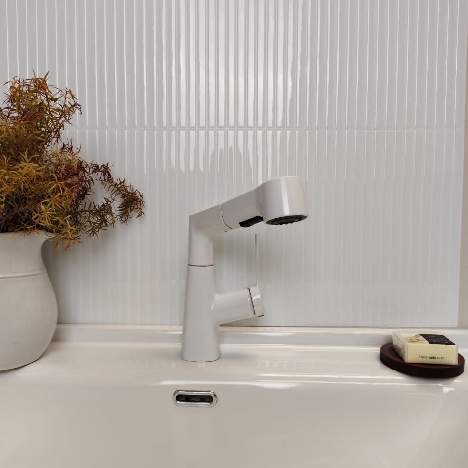 White bathroom faucet on a sink with a textured white wall in the background