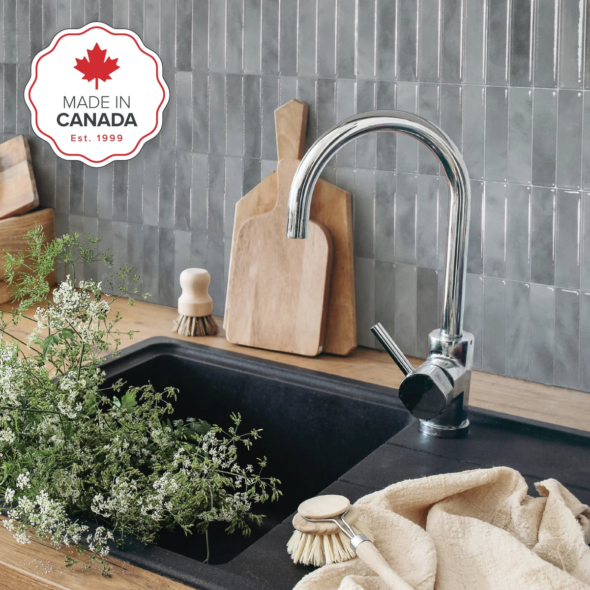 Kitchen sink with faucet, cutting boards, and cleaning supplies on a tiled wall background with &#39;Made in Canada&#39; logo.