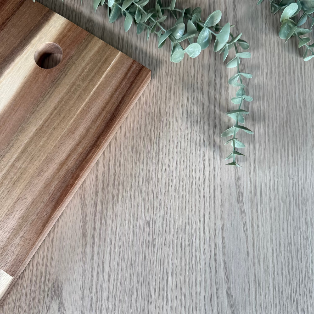 Wooden cutting board on a wooden adhesive vinyl with eucalyptus leaves.