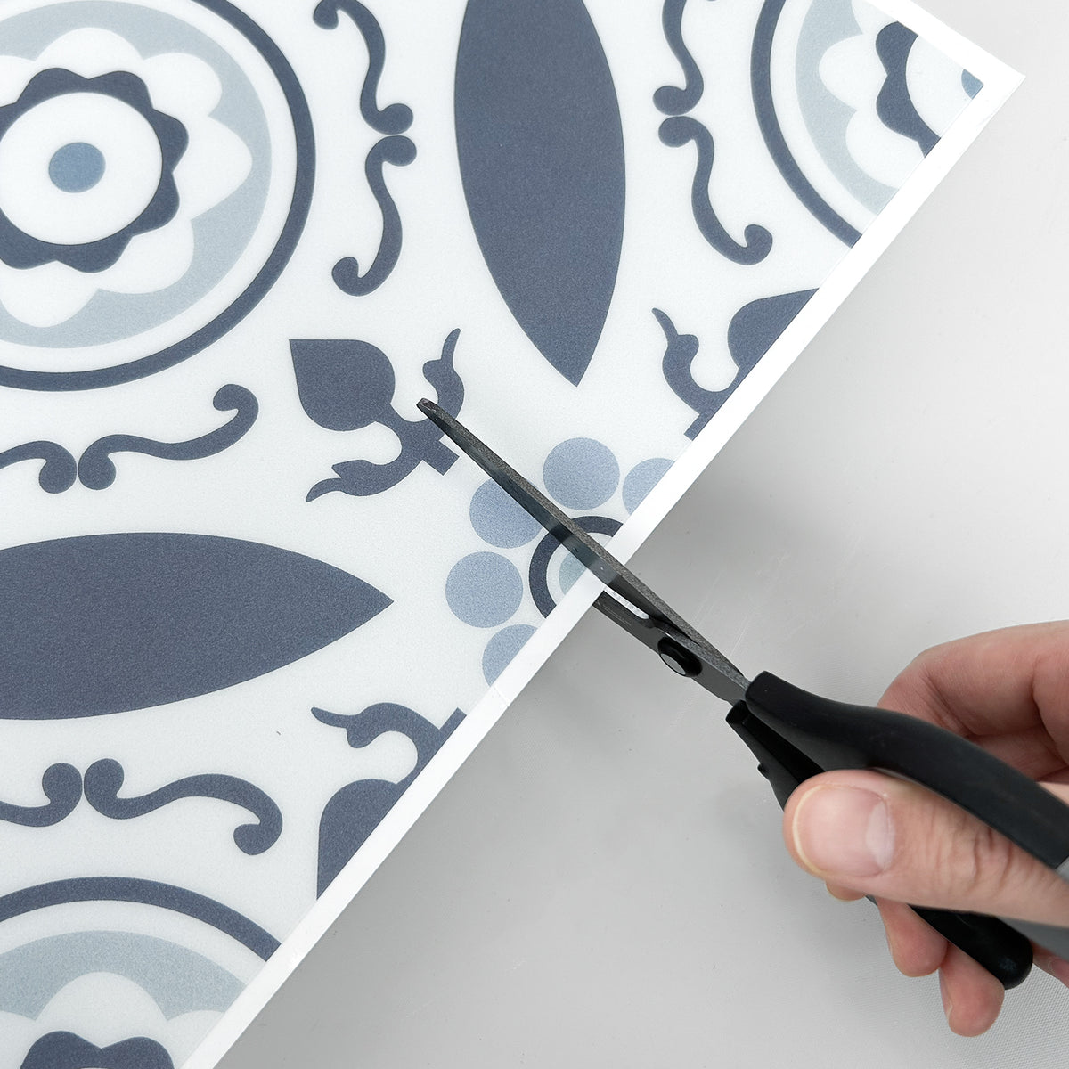Scissors cutting through a sheet of decorative vinyl floor tiles with a pattern on a white background