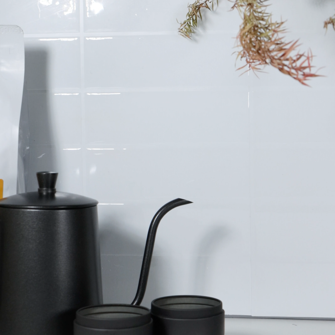 Black ceramic teapot and cups on a light gray surface with a white tiled wall in the background.