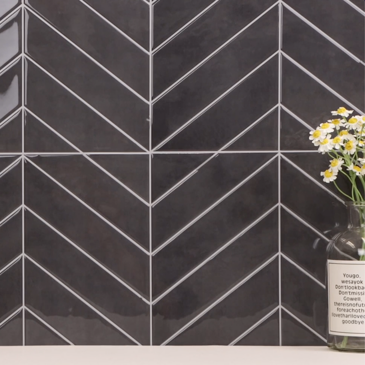 Black chevron patterned tiles with a vase of flowers on a white surface