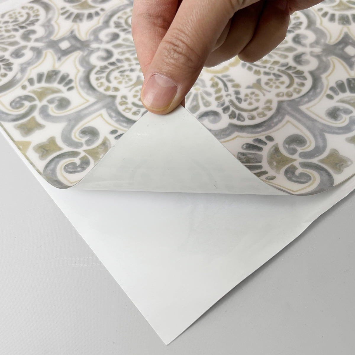 Hand peeling back a sheet of decorative floor tiles with a geometric pattern.
