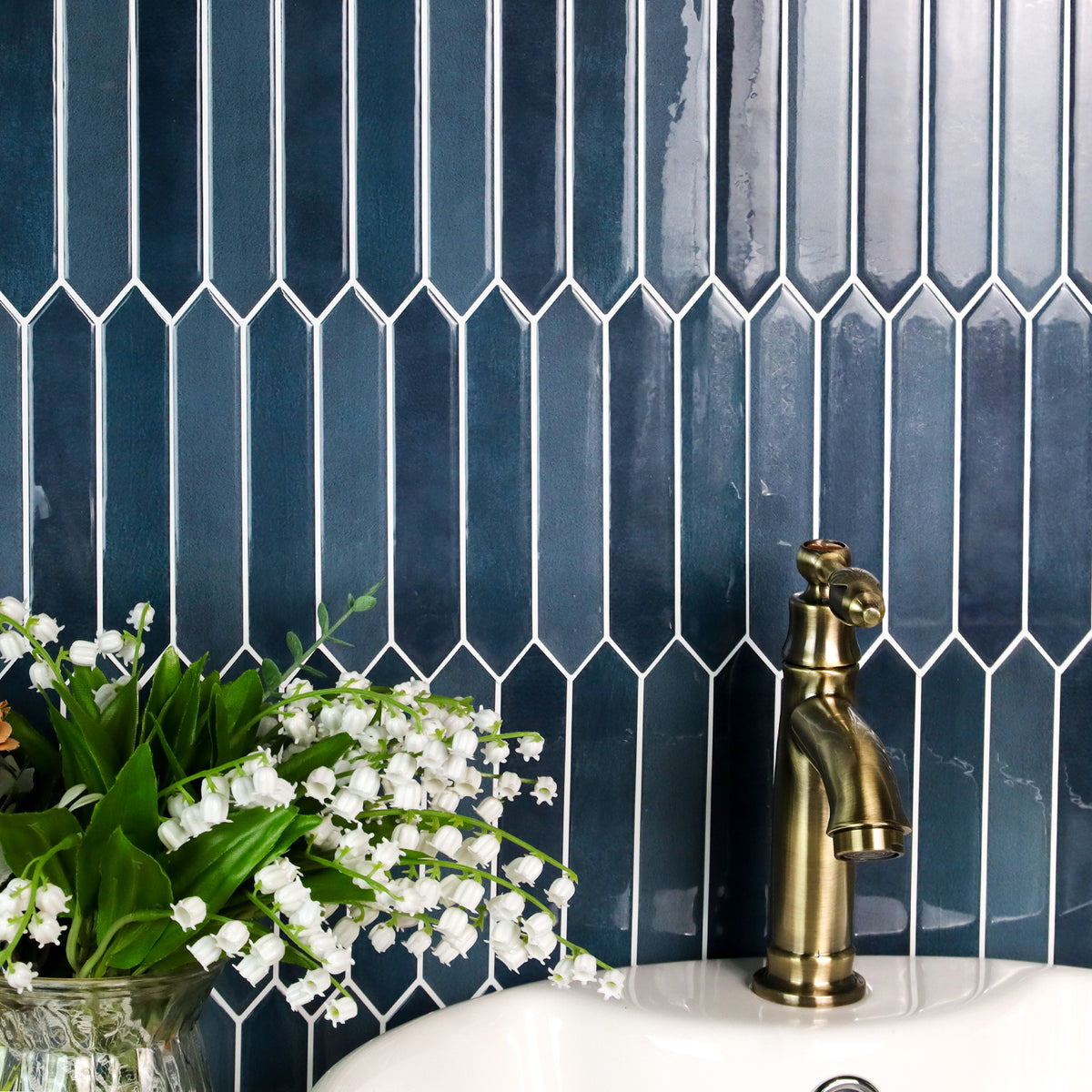 Blue tiled wall with a gold faucet and white flowers in the foreground