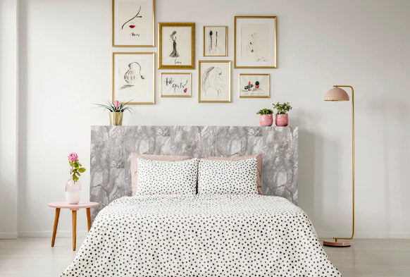 double bed with white bed clothes, marble flat headboard, pink side table to left and pink floor lamp t the right, picture frames above
