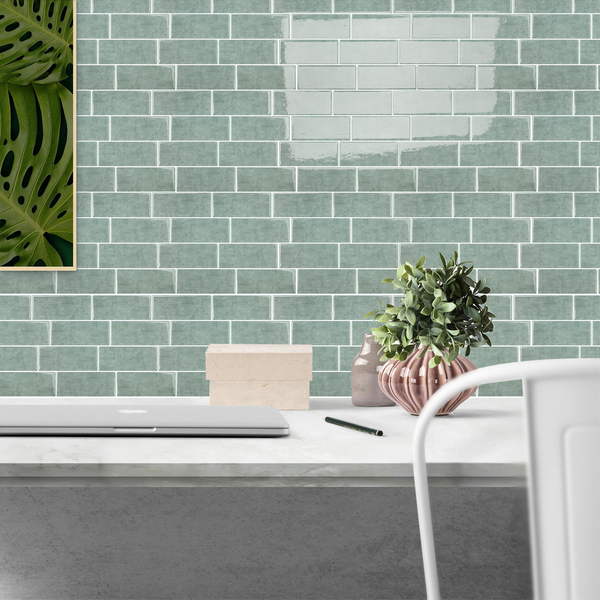 Modern office desk with laptop, plant, and decor against a green tiled wall.