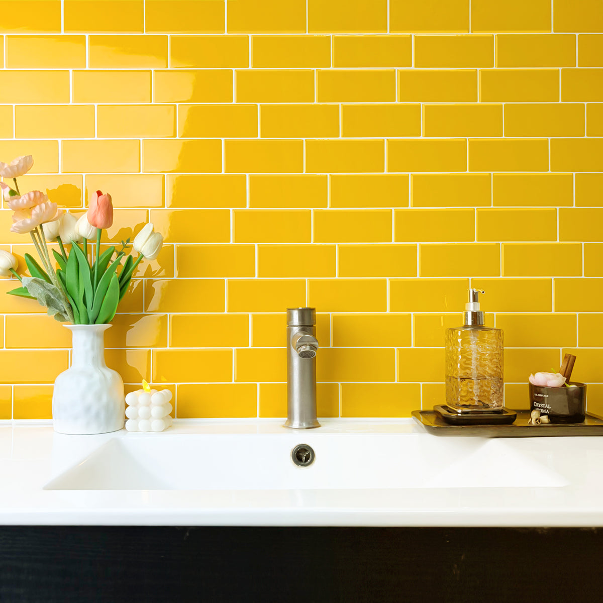 Bathroom sink area with yellow tiled wall and decorative items.