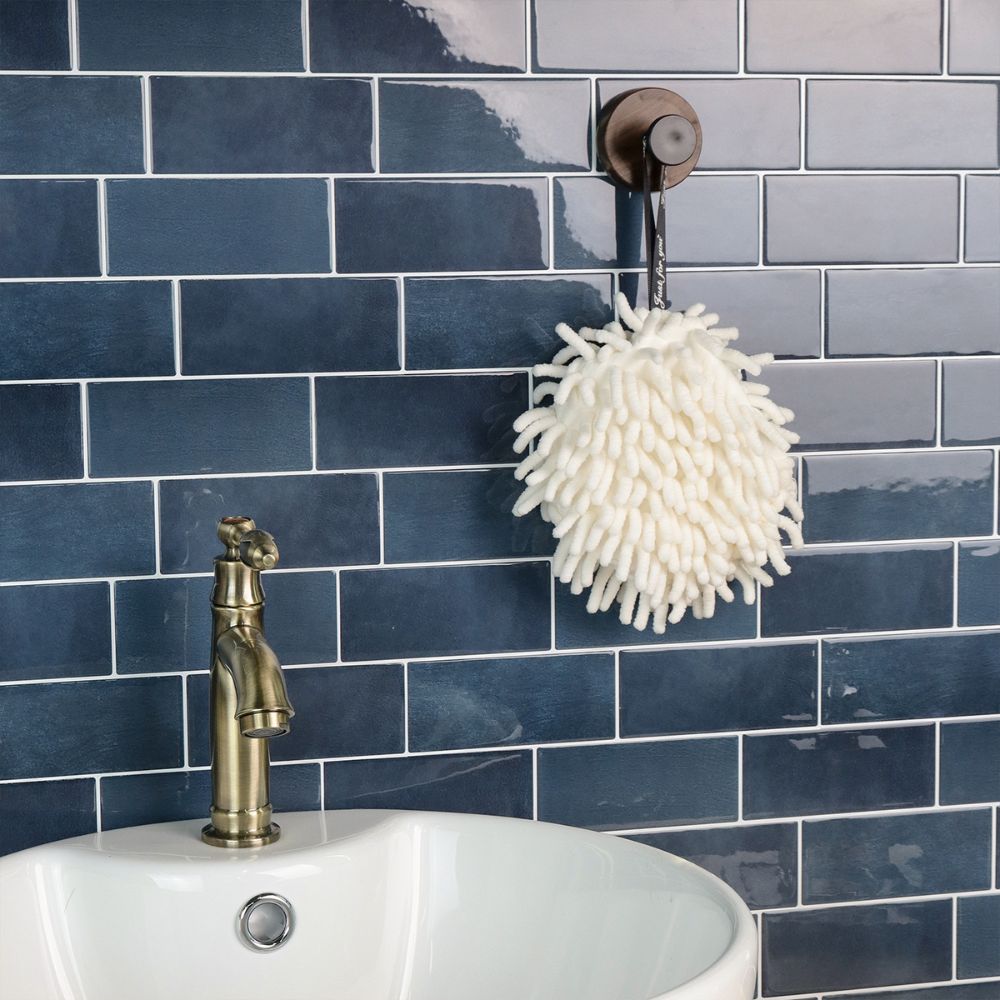 White hanging scrubber on a blue tiled wall with a sink and faucet.