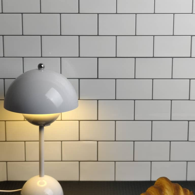 White lamp against a tiled wall with a white subway pattern