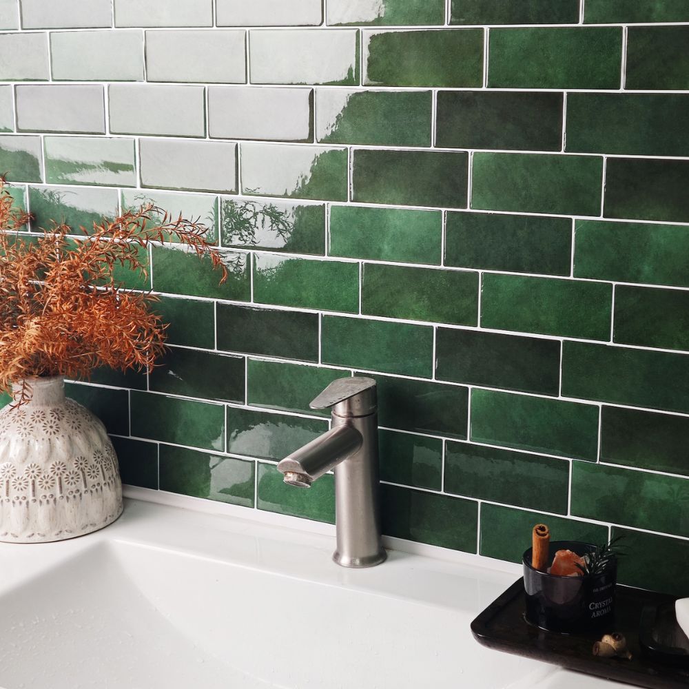 Green tiled wall with a silver faucet and decorative elements in a bathroom setting.