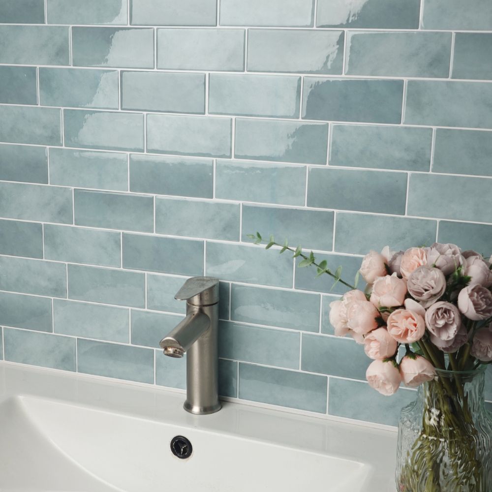 Bathroom sink with teal tiled wall and pink flowers in a vase.