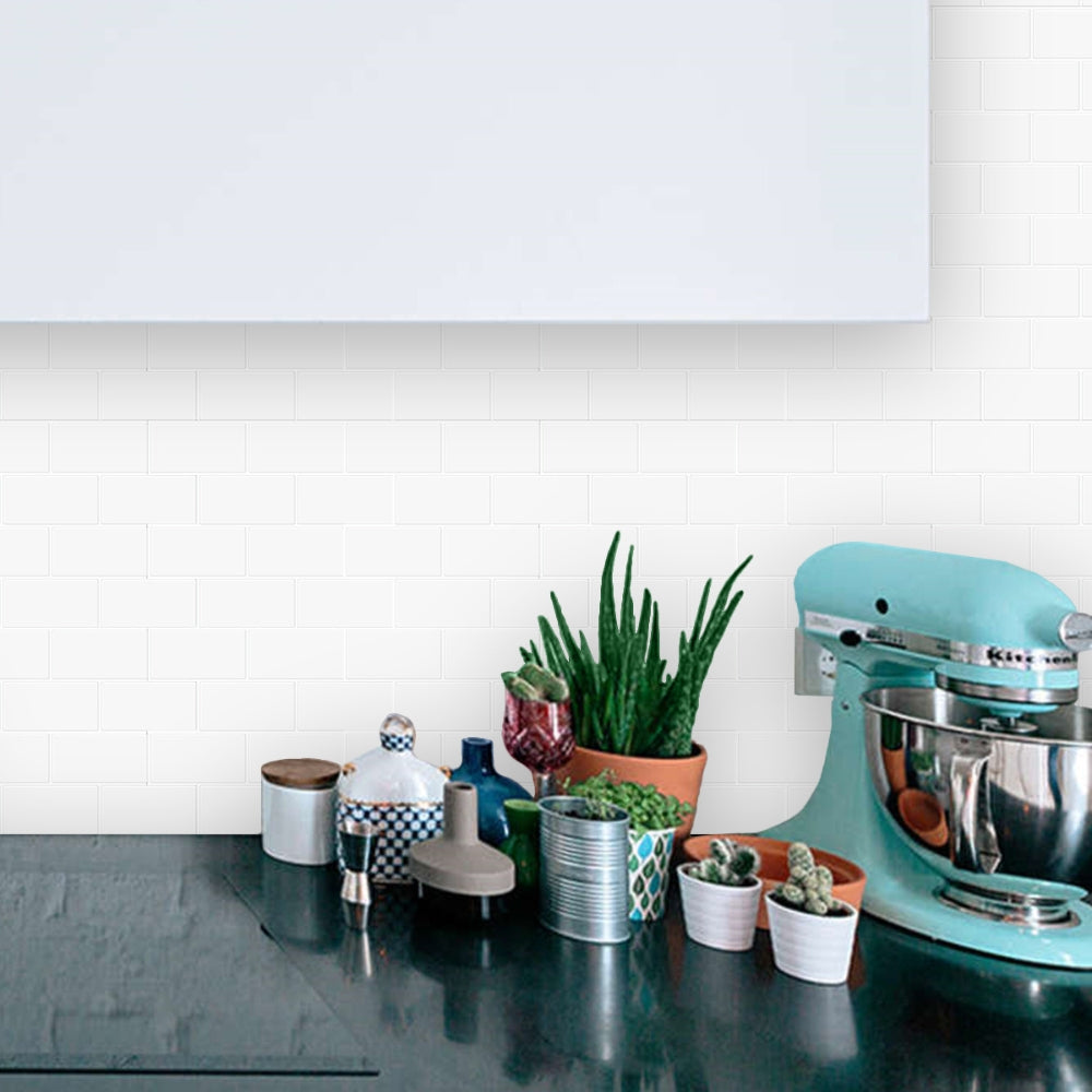 Teal stand mixer on a kitchen counter with potted plants and decorative items with white subway tiled background
