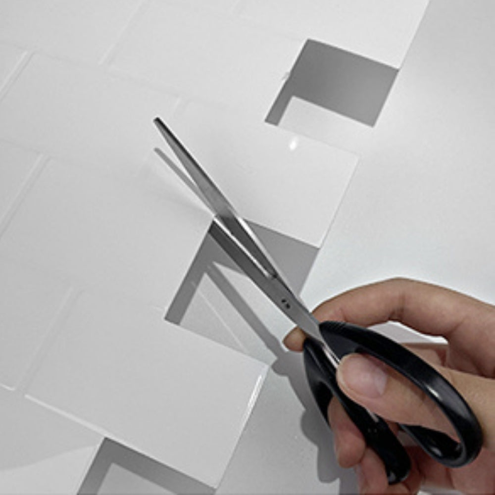 Hand holding scissors over white subway tile