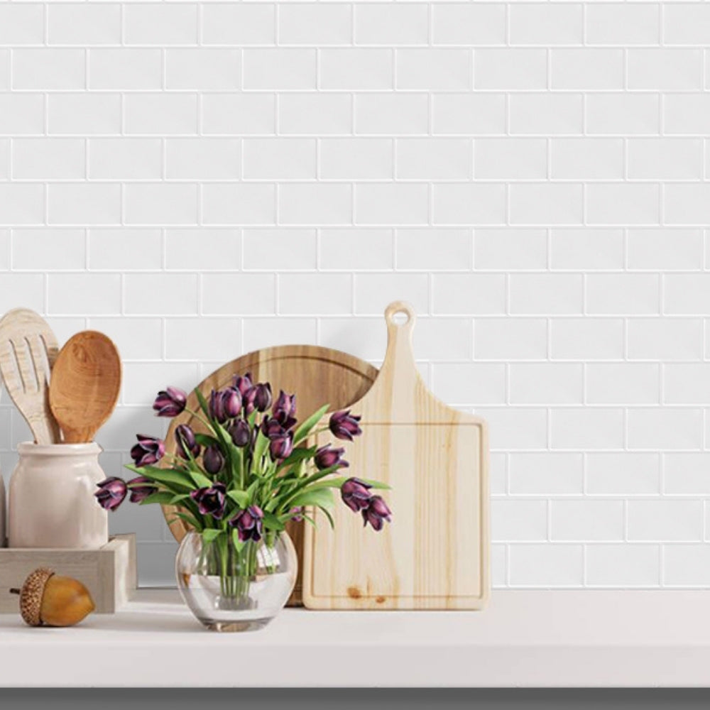 Kitchen counter with wooden cutting board, vase of purple tulips, and kitchen utensils against a white tiled wall.