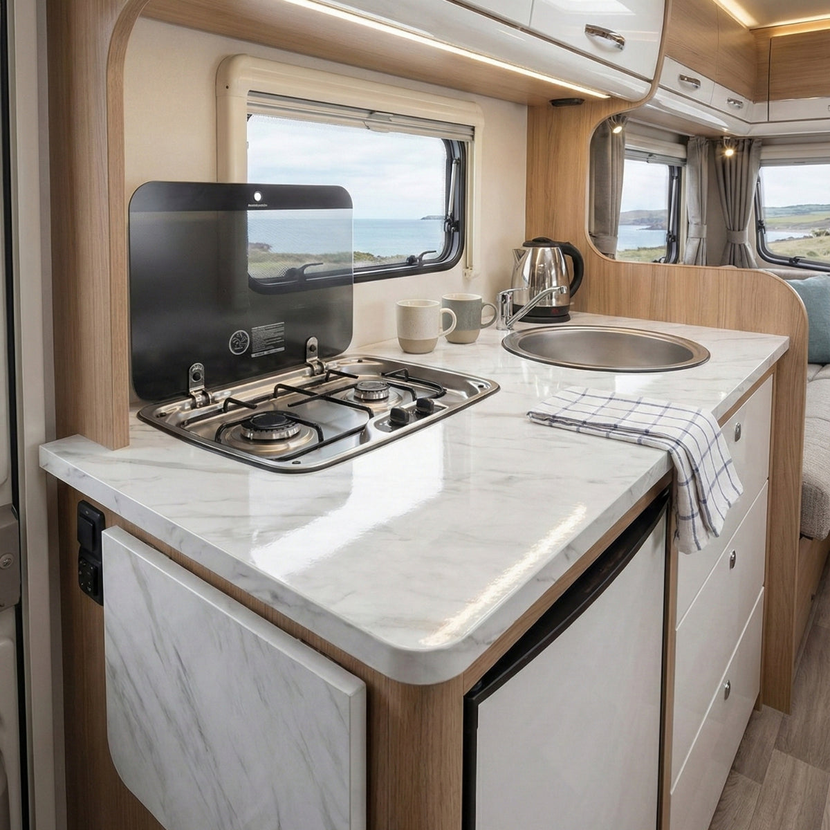 Compact kitchen area inside a caravan with stove, sink, and white marble wrapped countertop.