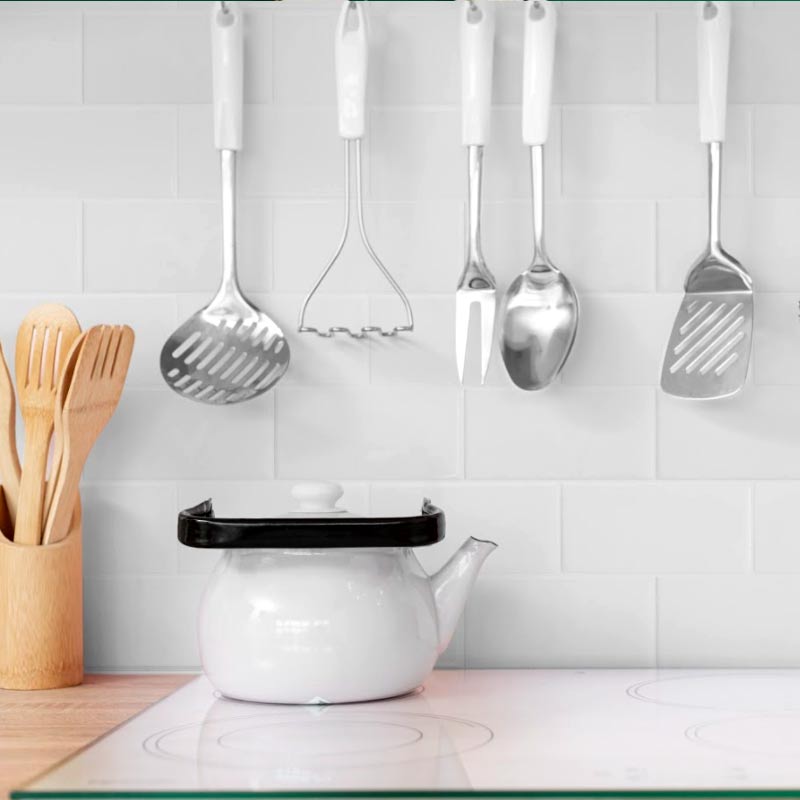 cooktop with white teapot and white subway tiles on wall and hanging down kitchen utensils