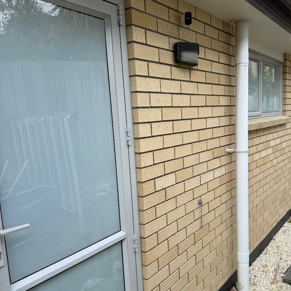 Beige brick wall with a frosted glass door and white pipe running vertically.