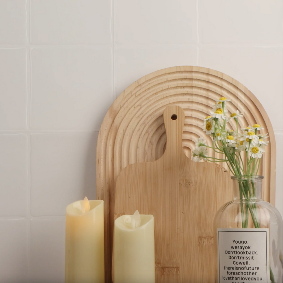 White square peel and stick tiles on wall with shopping board, candles and a vase of flowers