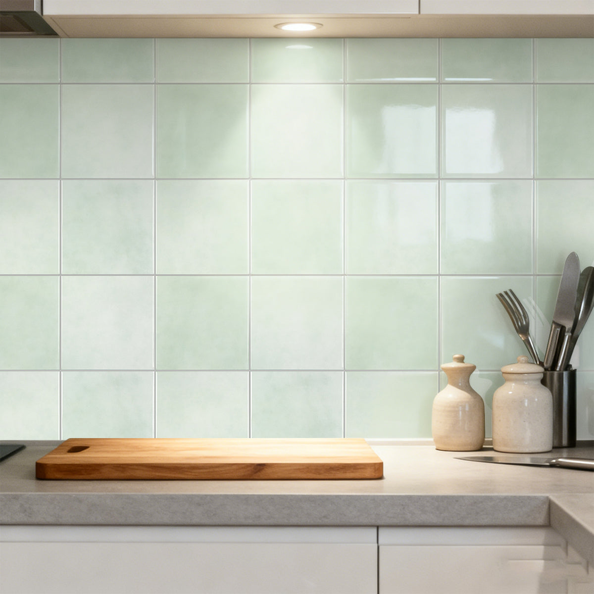 Modern kitchen with green tiled wall, wooden cutting board, and ceramic utensil holder.