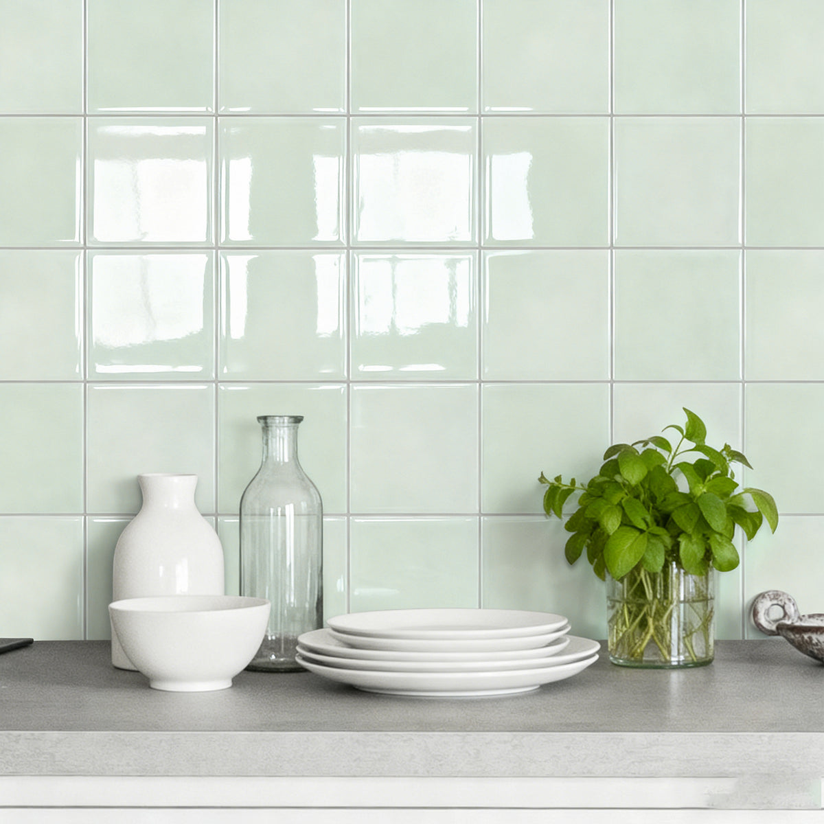 Kitchen counter with white dishes, a vase, and a plant against a light green tiled wall.