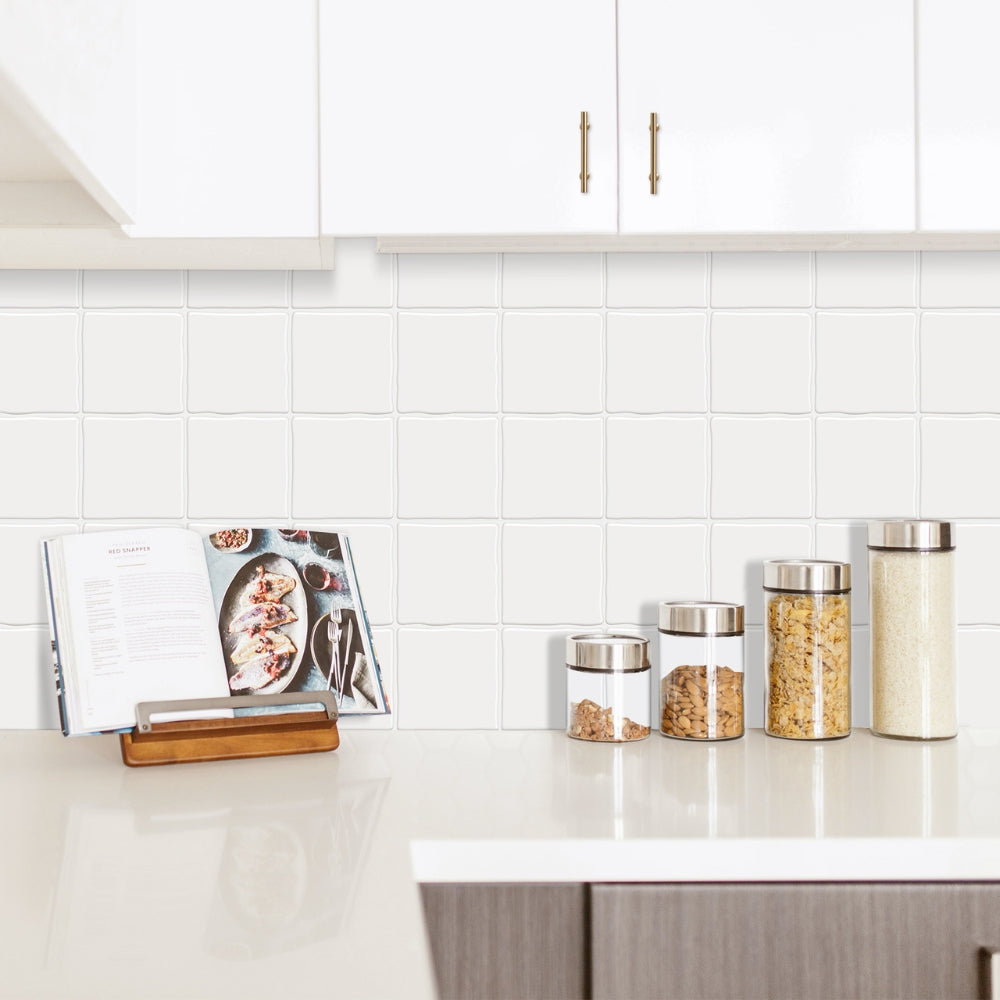 Kitchen counter with jars of snacks and a cookbook against a white tiled wall.