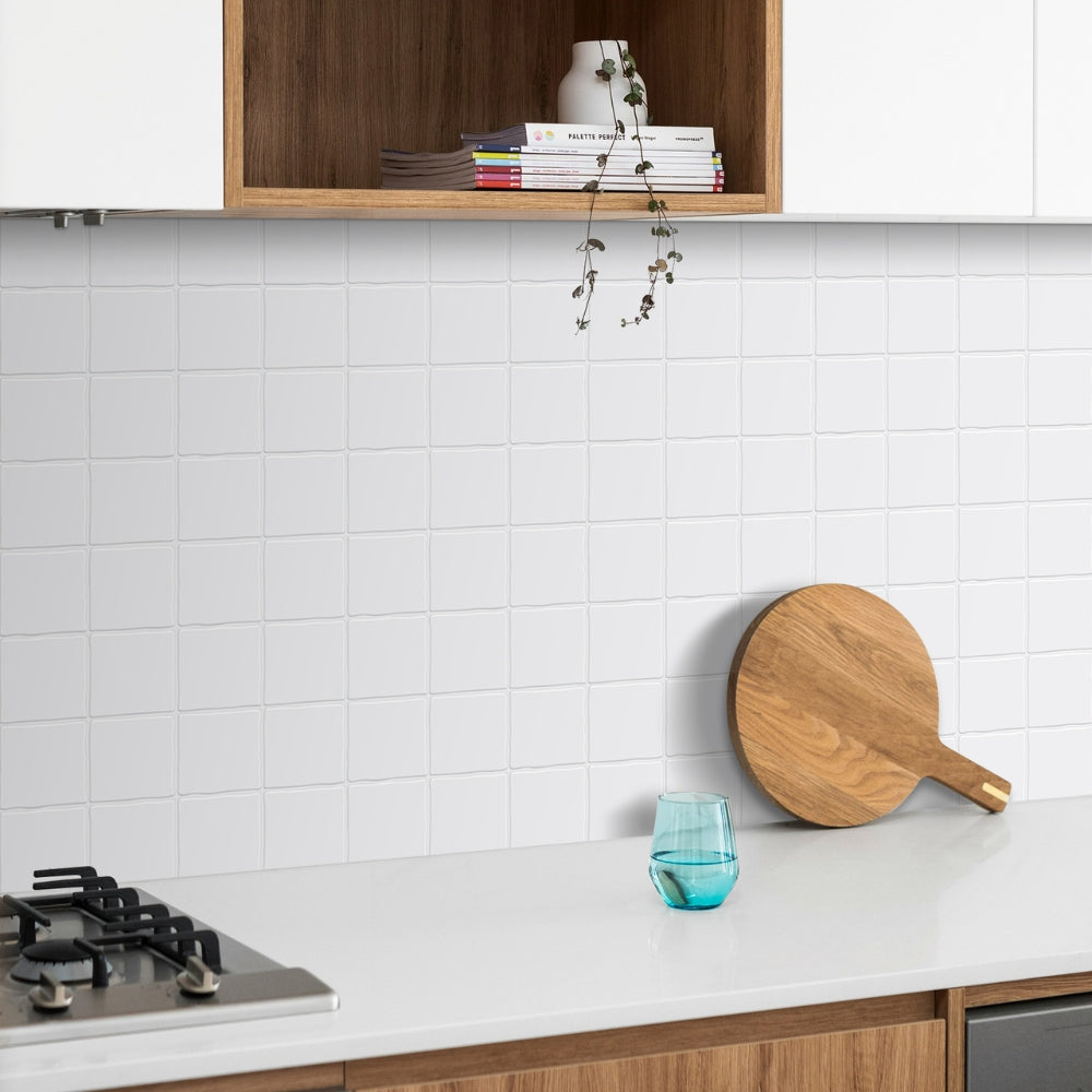 Modern kitchen with white tiled wall, wooden cutting board, and blue glass.