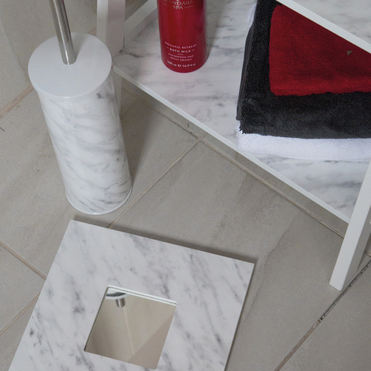 Bathroom setting with marble-patterned floor and shelf, featuring a red bottle and towels.