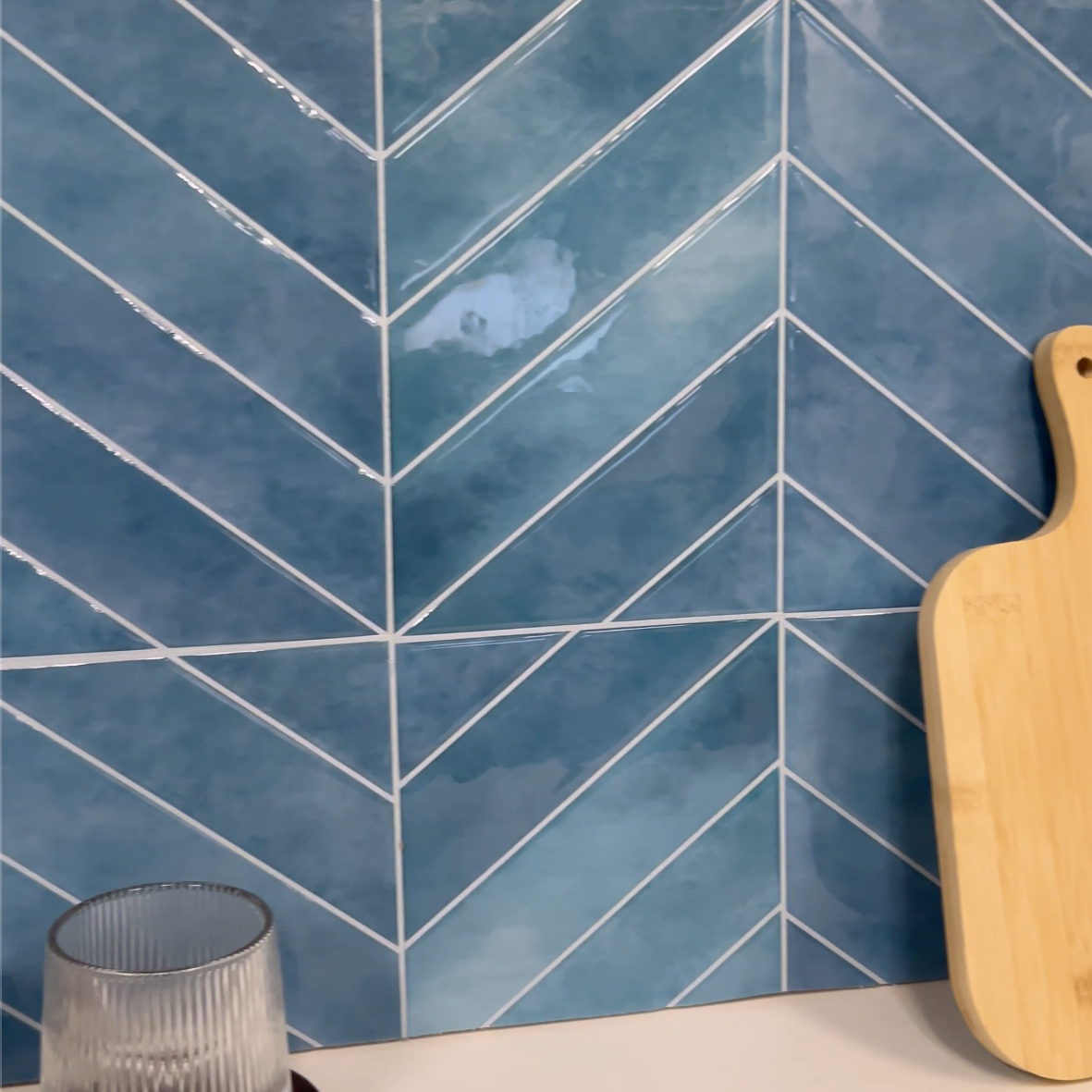 Blue tiled wall with a wooden cutting board and glass on a beige surface