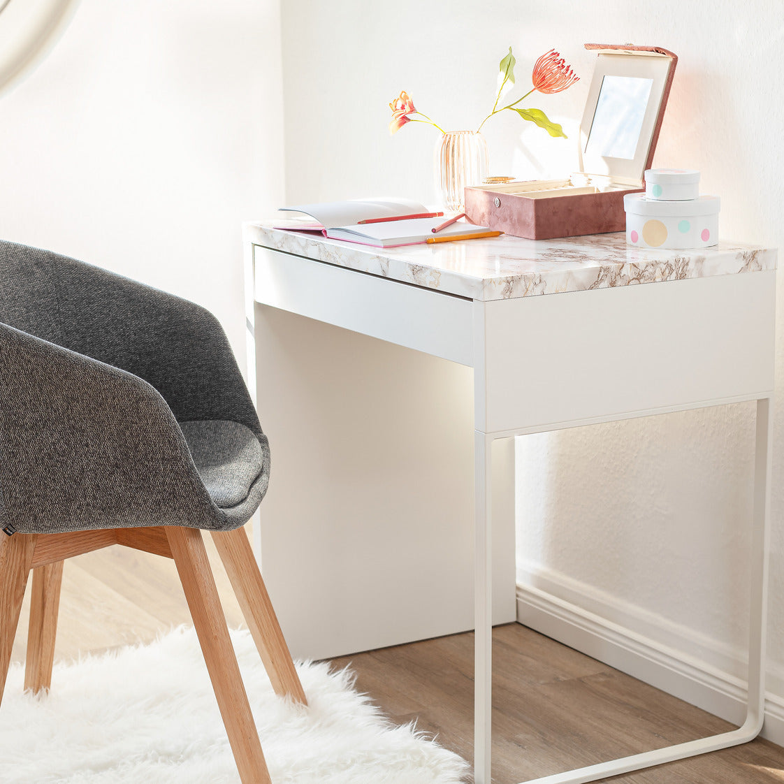 Gray chair in front of a white desk with decorative items on a light wood floor.