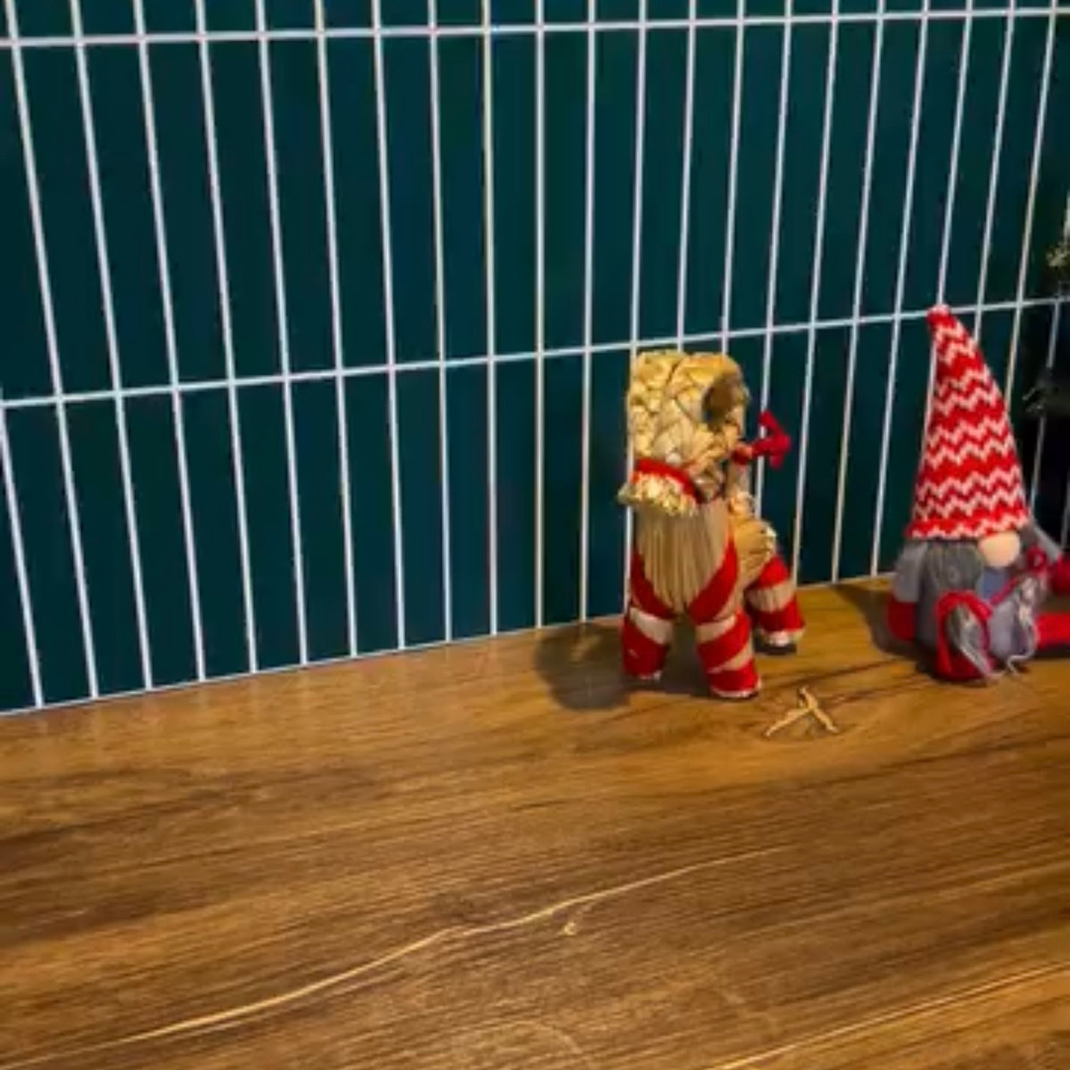 Two small figurines on a wooden surface with a dark tiled wall background