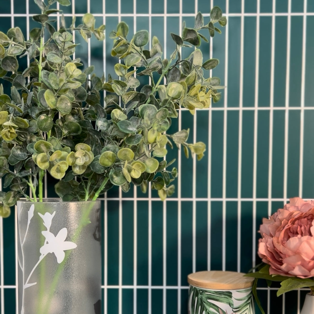 Vase with greenery and pink flower against a teal tiled wall