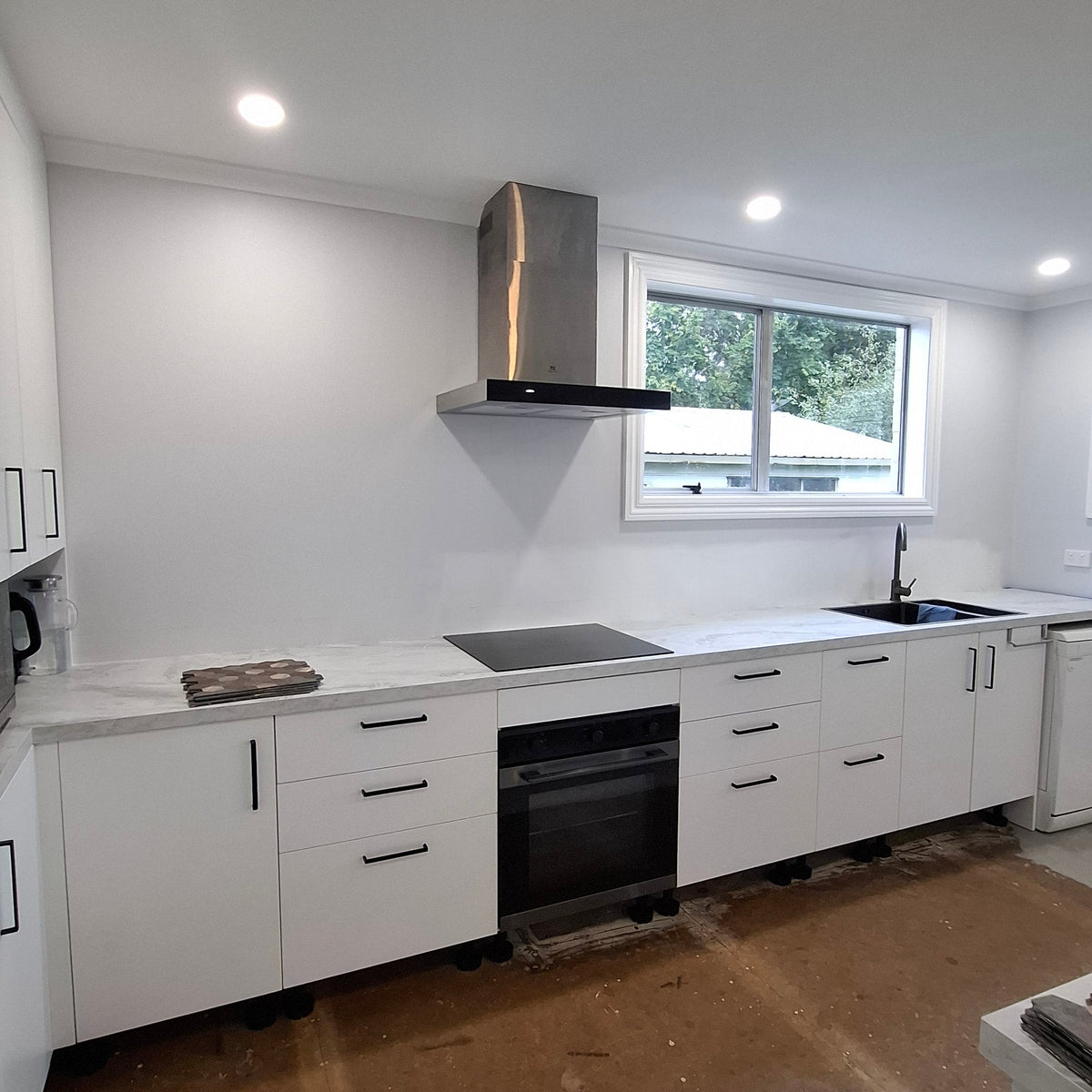 Modern kitchen with white cabinets, a window above the sink, and a cardboard box on the floor.