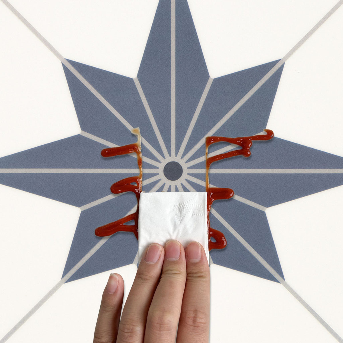 A hand holding a white napkin in front of a blue starburst pattern on a white background, with ketchup smeared across the center.