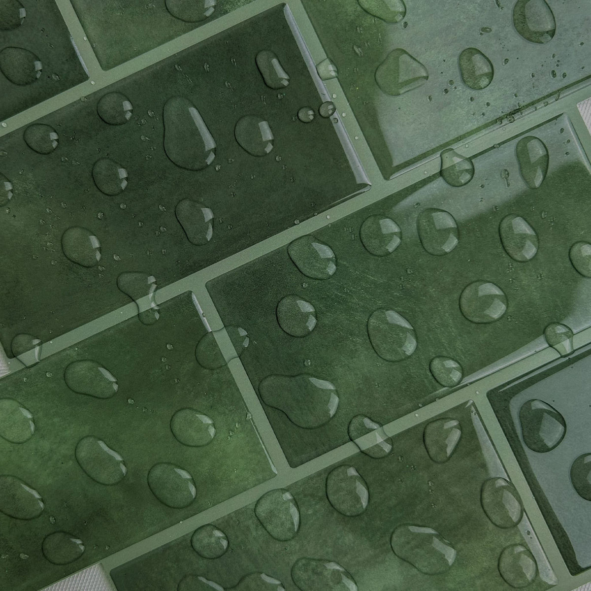 Close-up of green rectangular glossy tiles with water droplets on the surface, showing a wet textured finish.