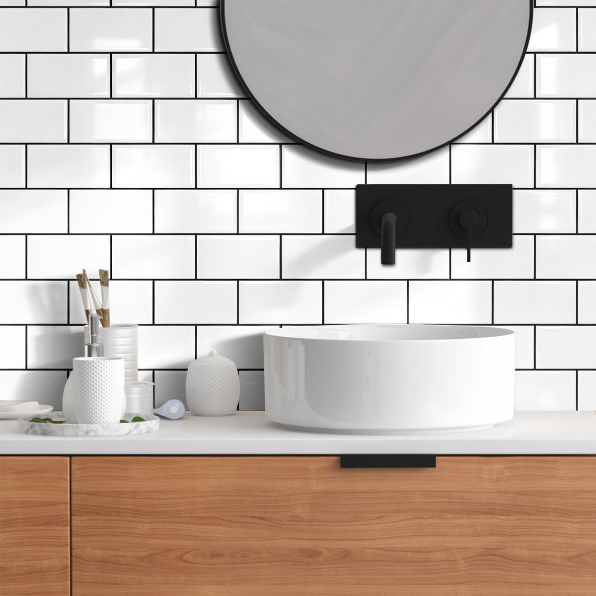 White subway tiles with almost black grout lines behind a wooden bathroom vanity and a round mirror