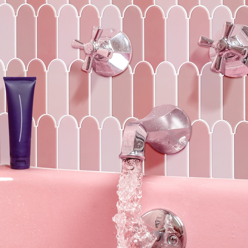 Pink bathtub with running water, purple tube of soap, and pink shampoo bottle against a pink background.