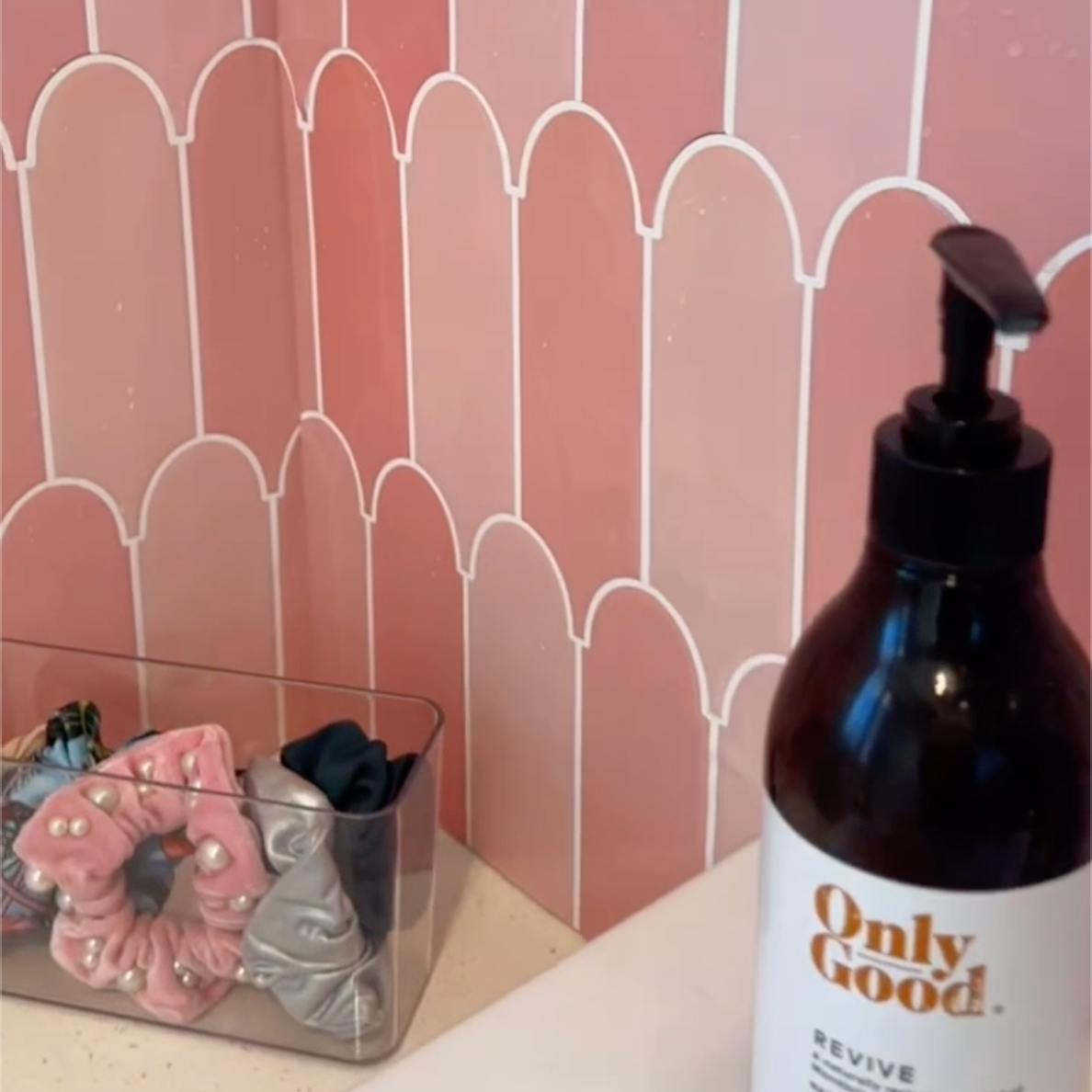 Brown bottle labeled &#39;Only Good&#39; on a counter with pink feather tiles in the background.