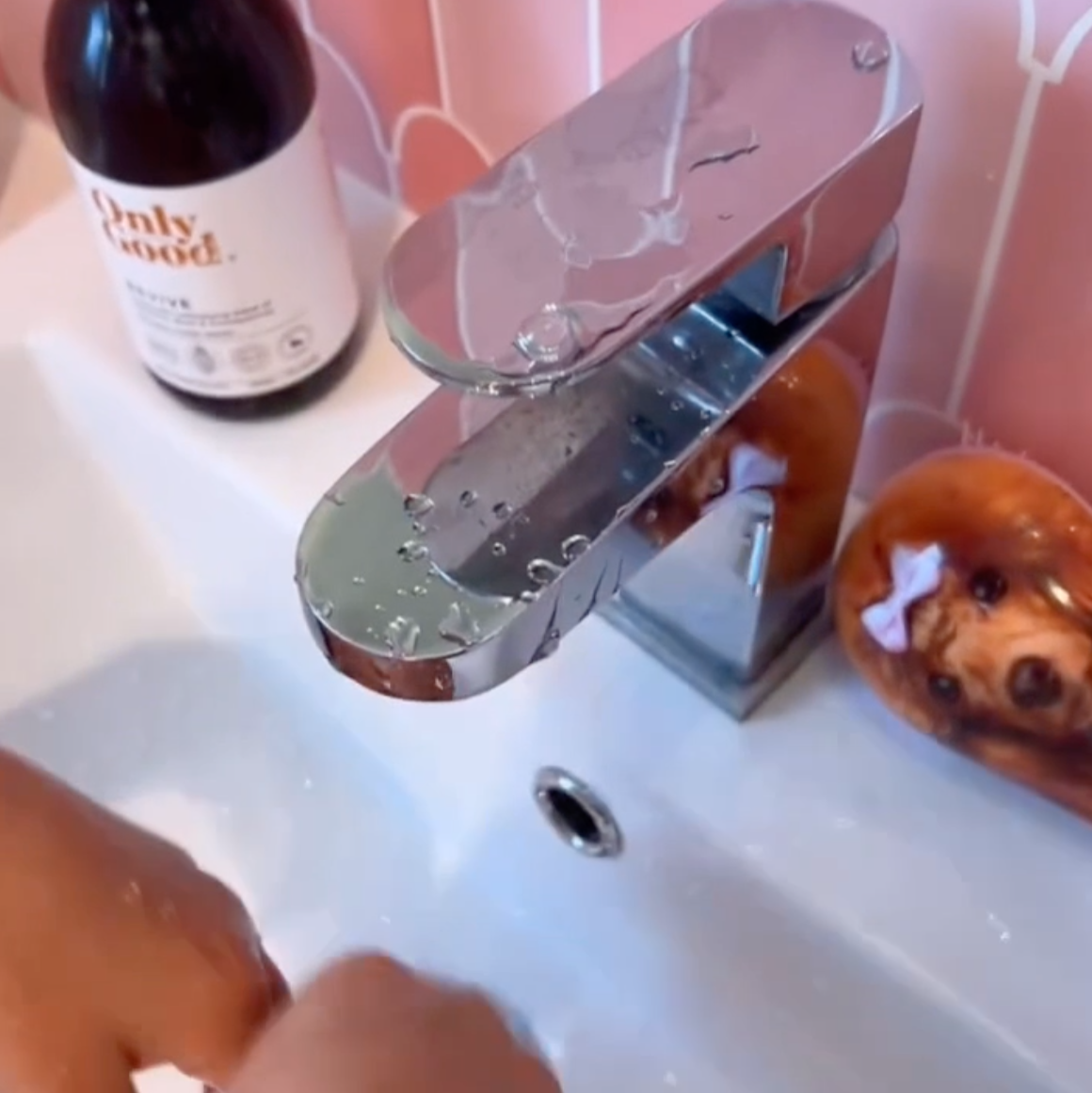 Chrome faucet on a sink with a bottle of soap and a decorative pink tiles in the background.