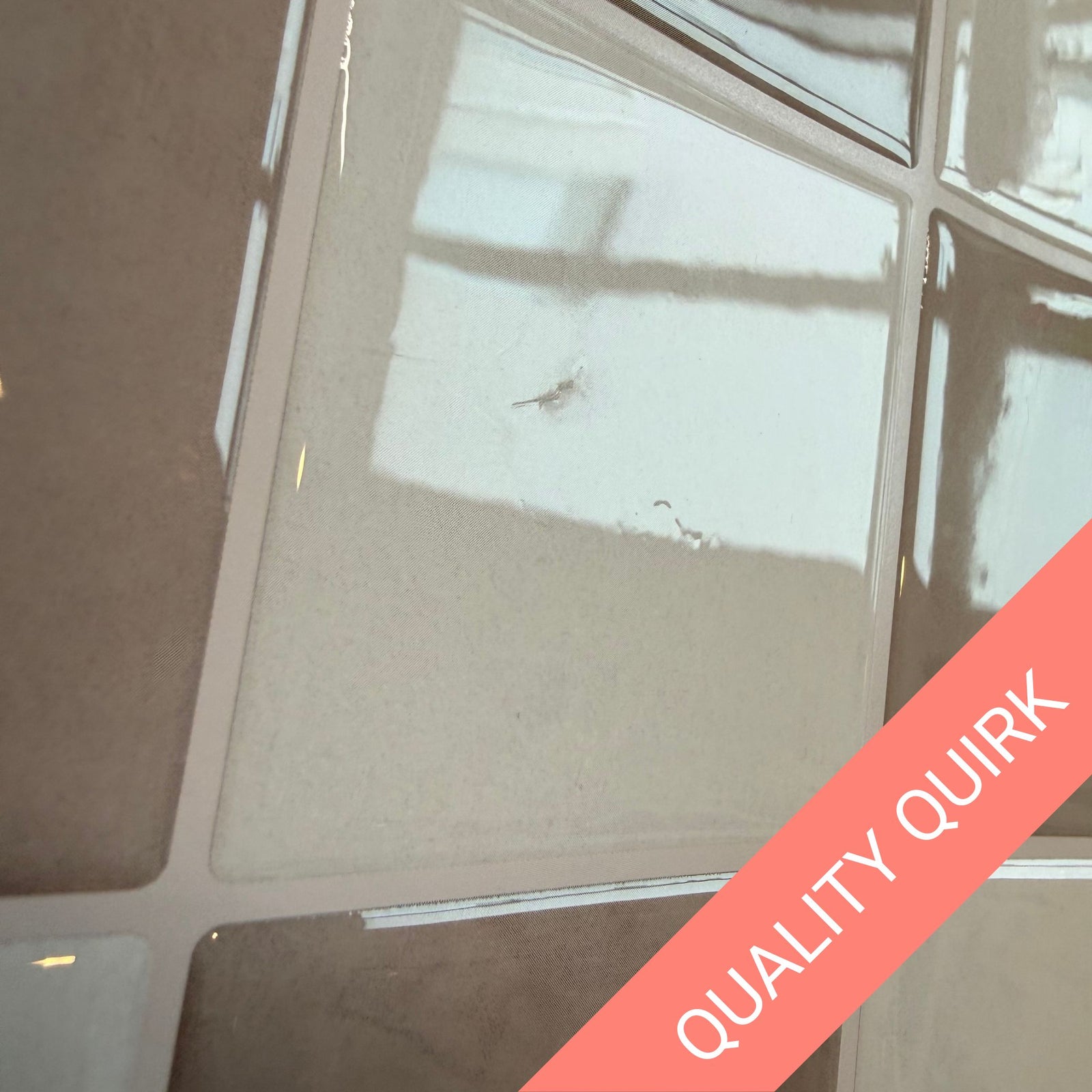 A glossy square tile sheet with a grid of 12 tiles in alternating light gray, white, and taupe-brown shades, shown on a speckled countertop with a coral diagonal banner reading 'QUALITY QUIRK'.