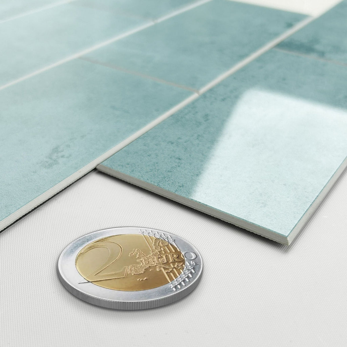Mottled light blue-green composite tiles shown in a close-up with a two-euro coin for scale on a white surface
