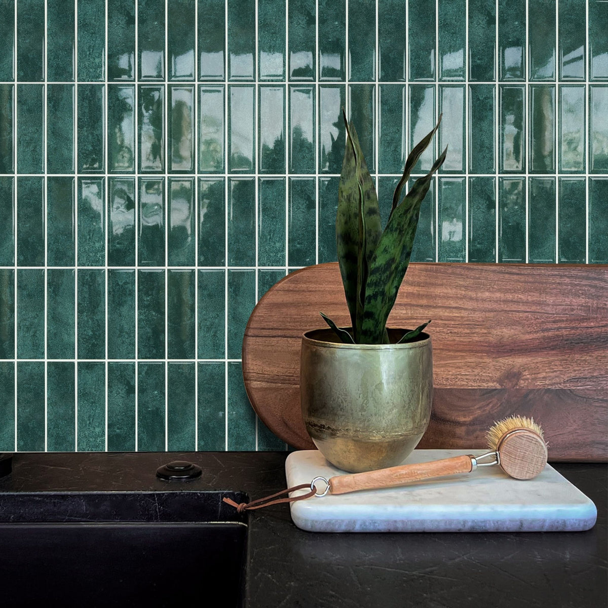 Emerald green stacked subway tiles on a wall behind a kitchen benchtop with a wooden cutting board and a plant.