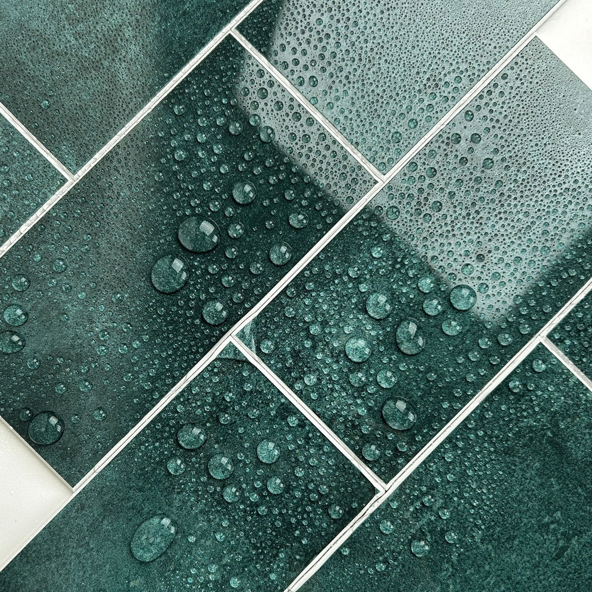 Dark teal green ceramic or porcelain tiles arranged in a stacked subway pattern, covered with water droplets to demonstrate water repellency.