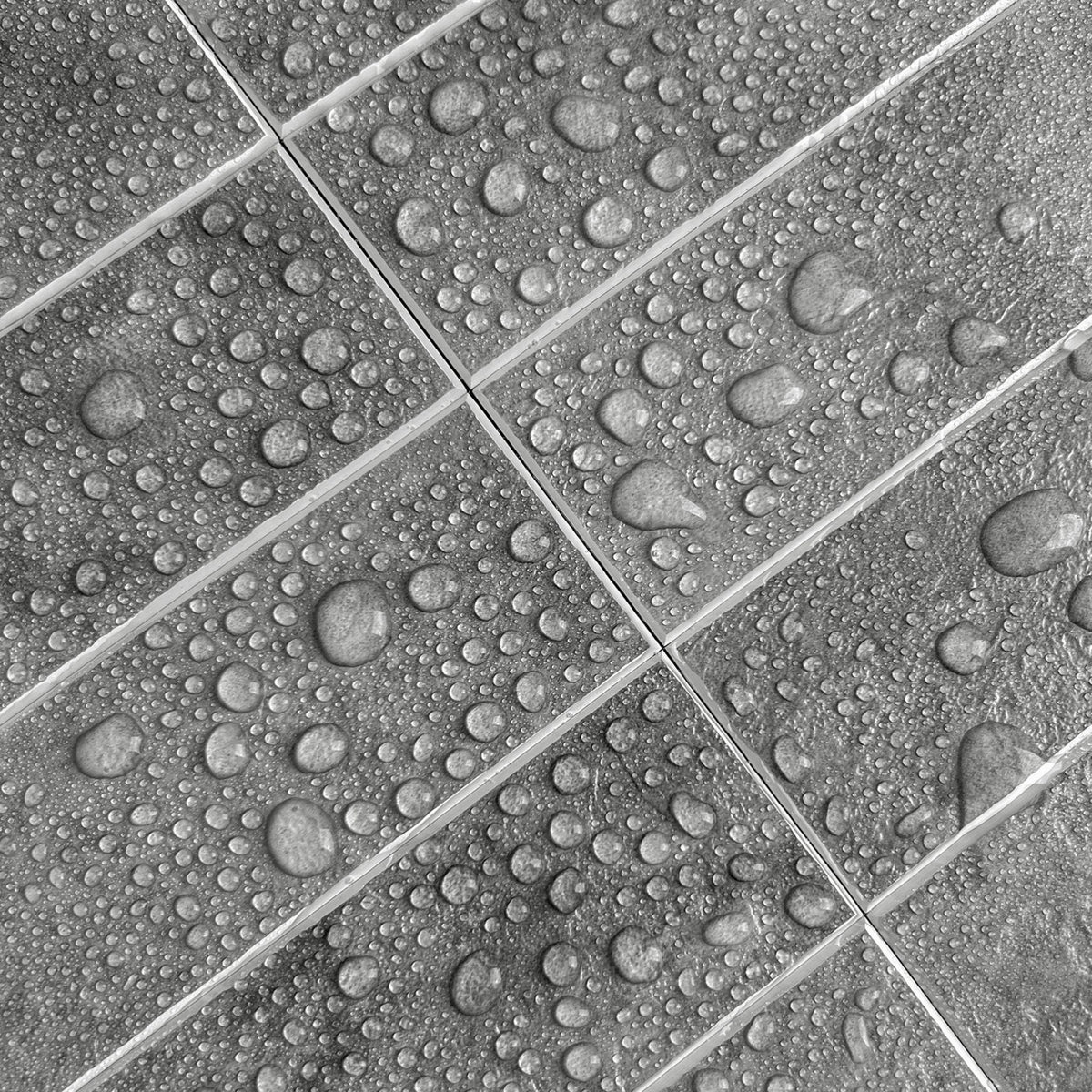 Gray stone-look rectangular tiles with a glossy finish, covered in water droplets that bead on the surface, arranged in a diagonal grid pattern.