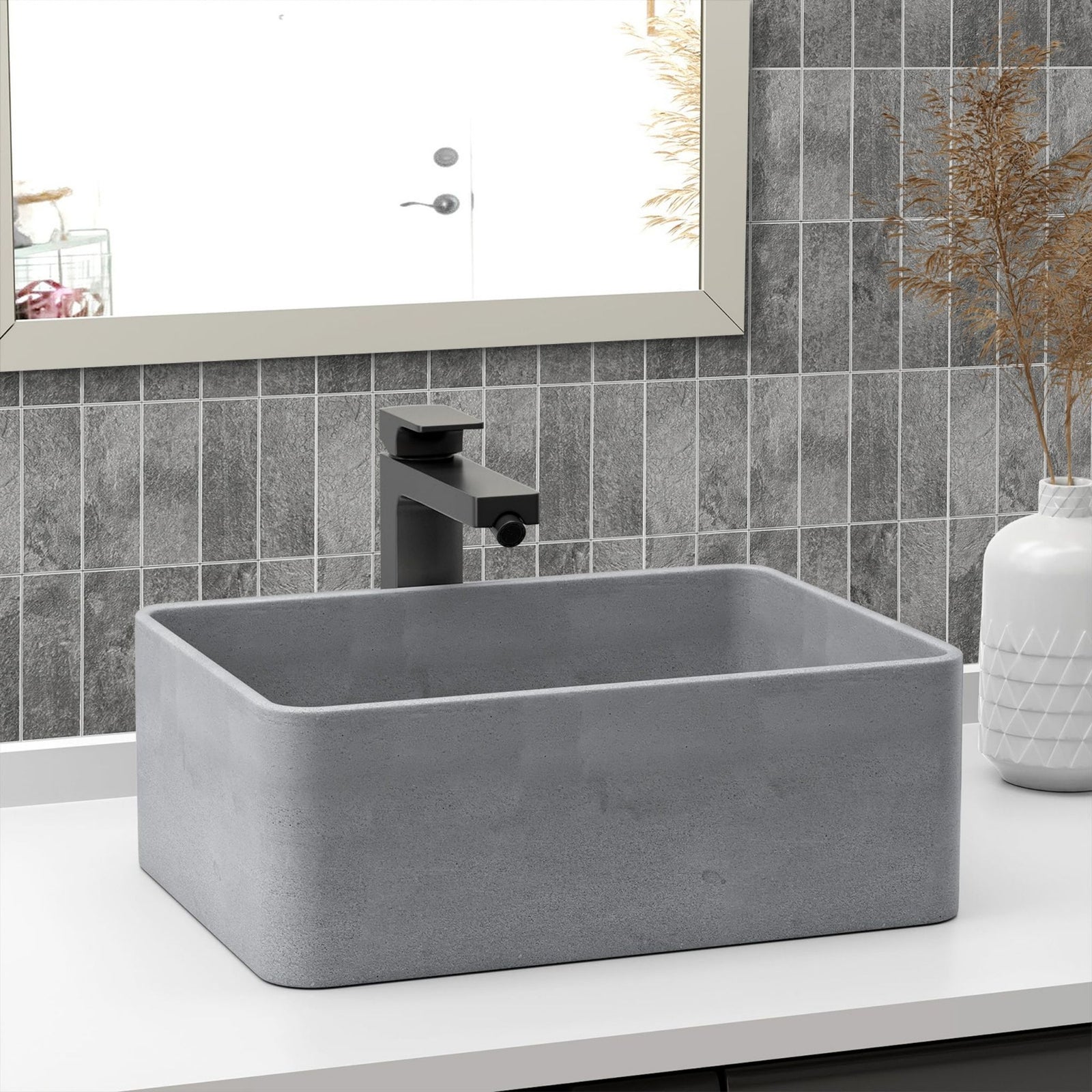 A rectangular grey concrete bathroom vessel sink with a matte black faucet, set on a white countertop against a grey tiled backsplash.